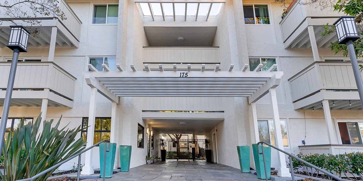 Entrance to a modern white apartment building with balconies, a pergola, and decorative potted plants, numbered 175.