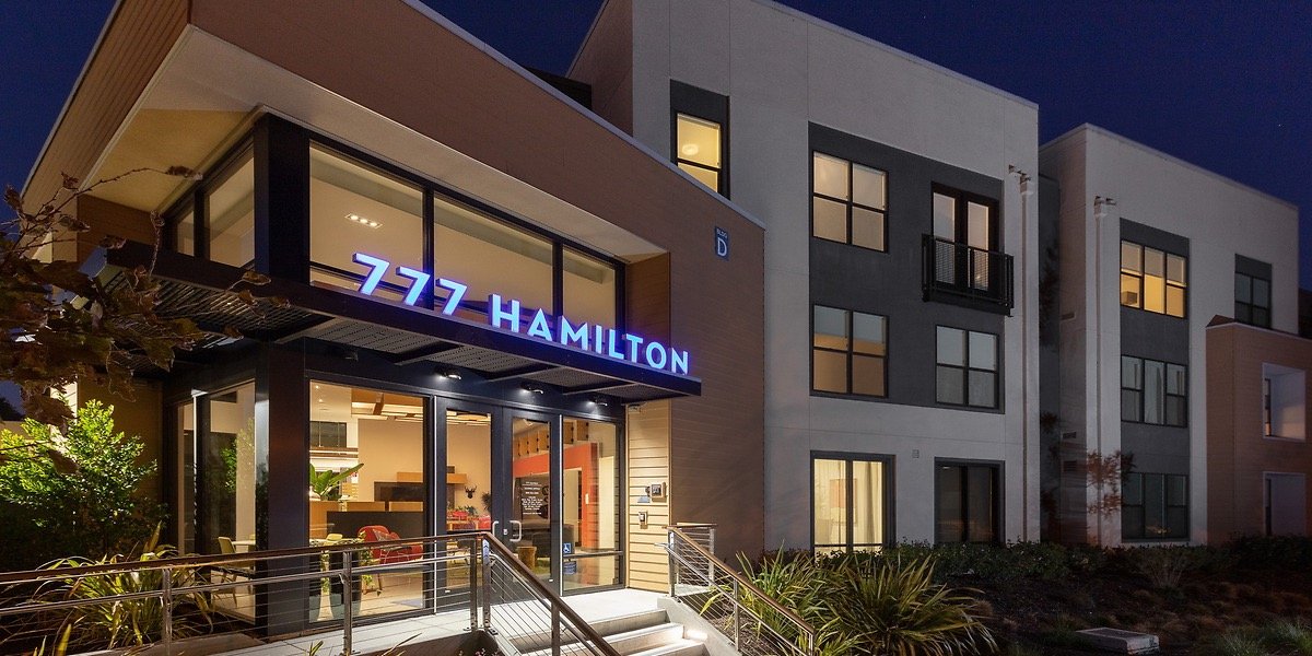 Night view of a modern apartment building with a lit sign that reads "777 HAMILTON" above the entrance