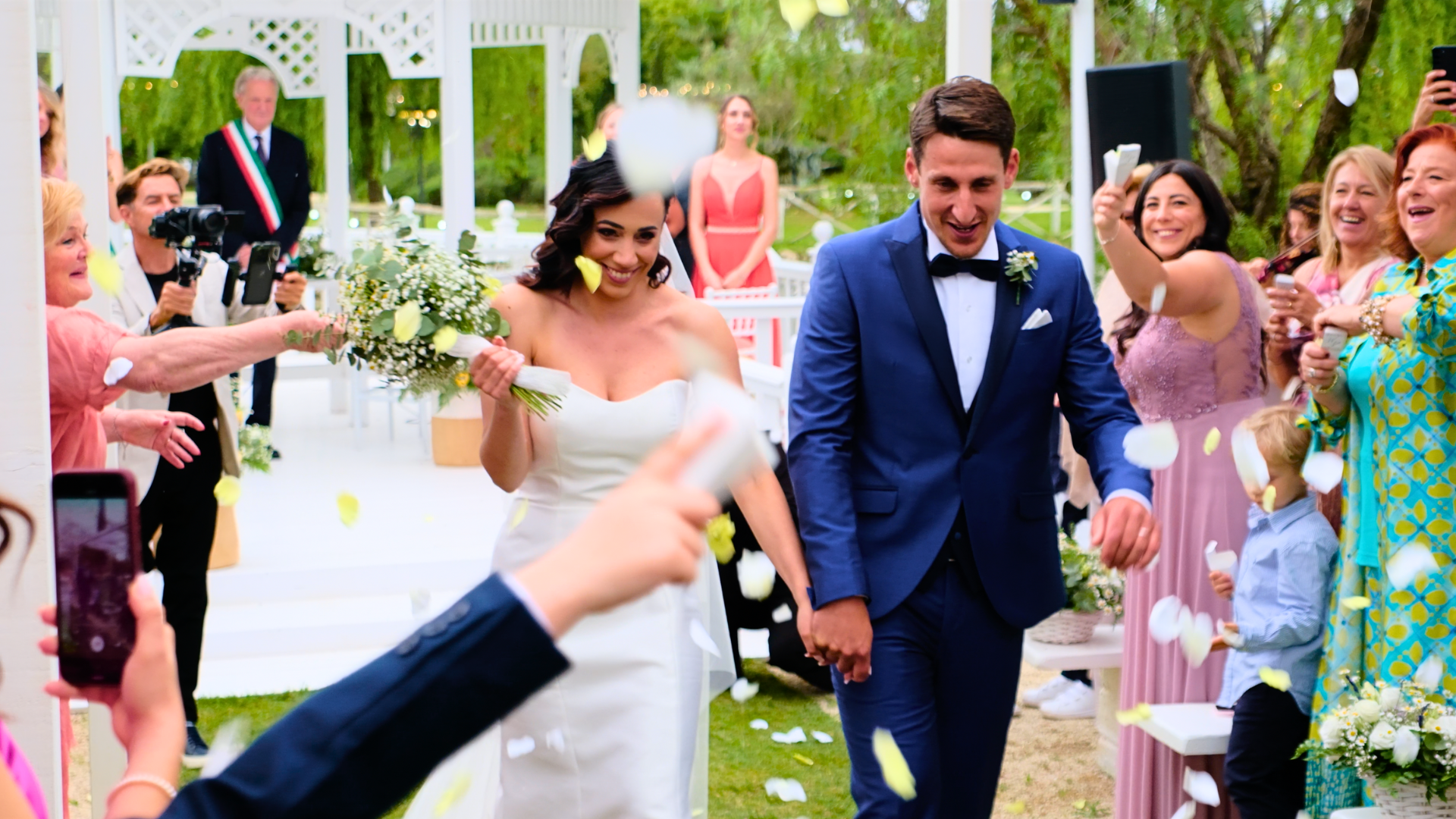 Sposi che sfilano sotto una pioggia di petali e coriandoli dopo la cerimonia all'aperto. Musica e intrattenimento per matrimoni da sogno con MDM Eventi