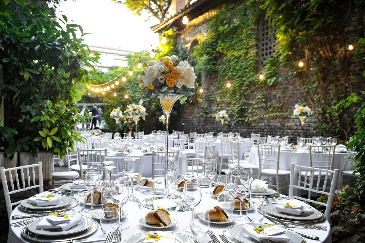 Allestimento tavoli imperiali per matrimonio all'aperto presso il Castello della Spizzichina, con centrotavola floreali e luci calde.