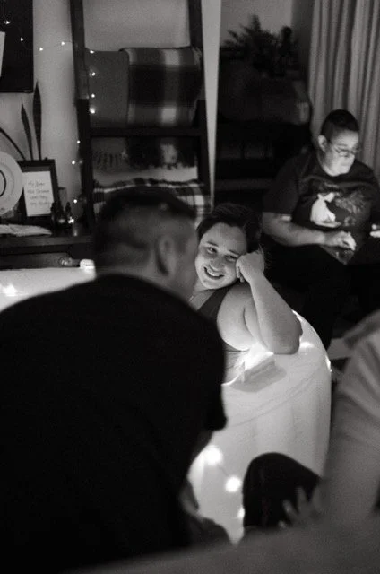 People socializing in a cozy indoor setting with soft lighting, including a woman smiling and a man with his back to the camera.