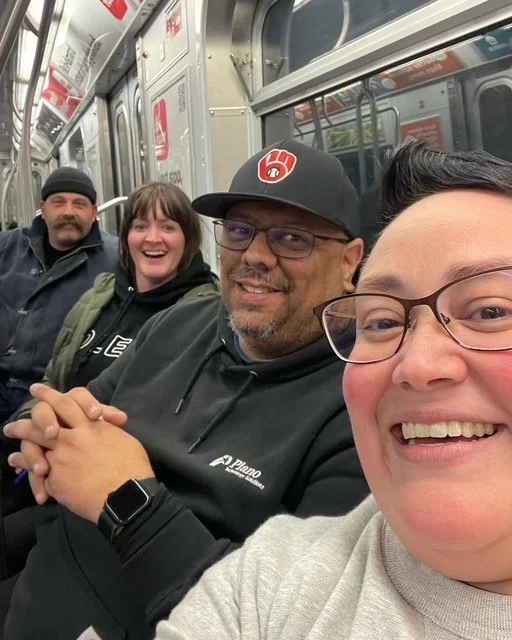 Four people sitting together on a train, smiling at the camera.