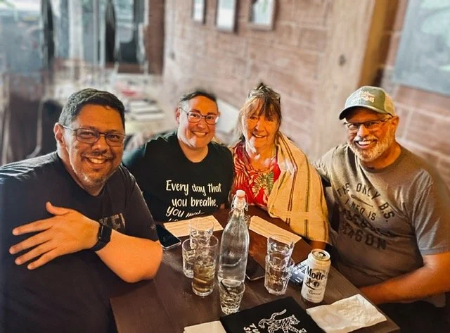 Family of four sitting at a restaurant table smiling, with drinks.