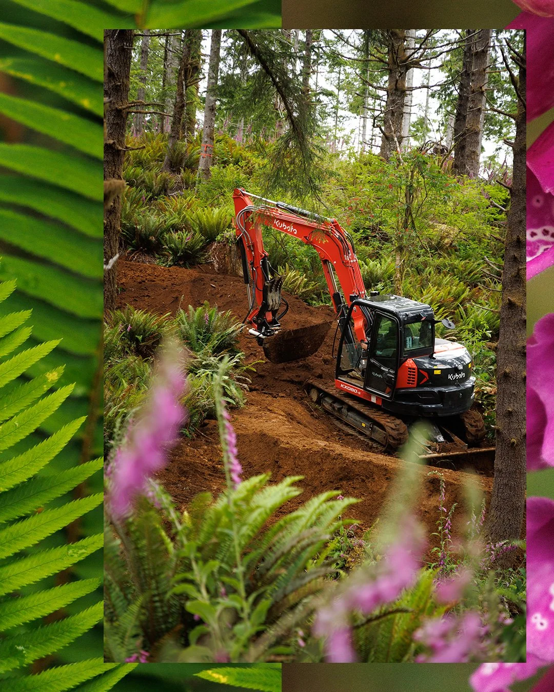 A small red Kubota excavator digging into brown soil in a lush forest with tall trees and green foliage, framed by pink and green plants.