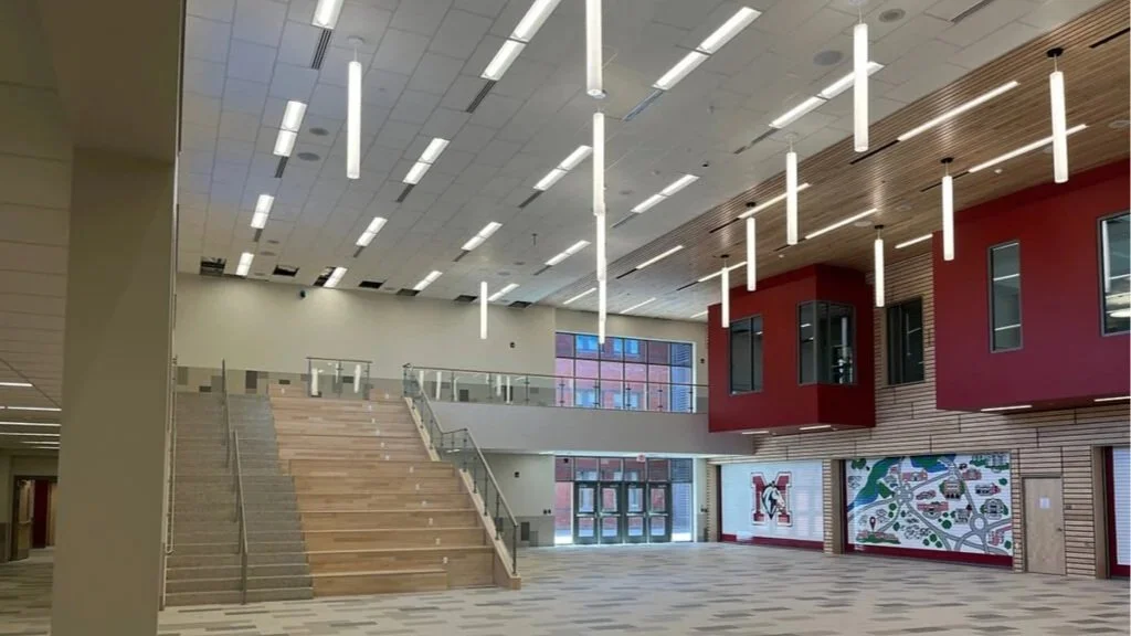 Interior of a modern school or auditorium with stairs, multiple windows, and colorful wall art.