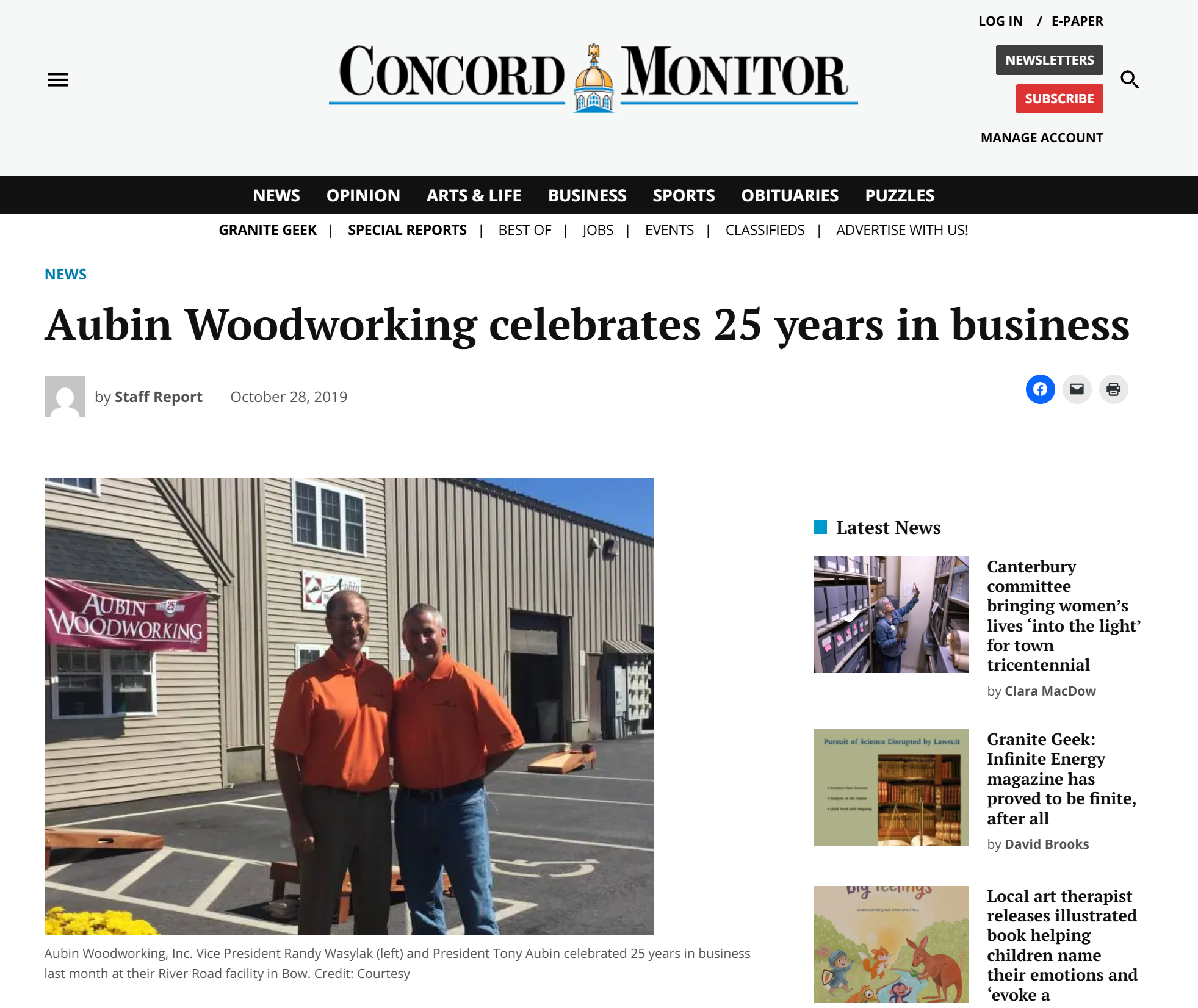 Two men in orange shirts standing outdoors in front of a beige building with a sign that reads "Aubin Woodworking" and a red banner. One man is slightly taller, and both are smiling.