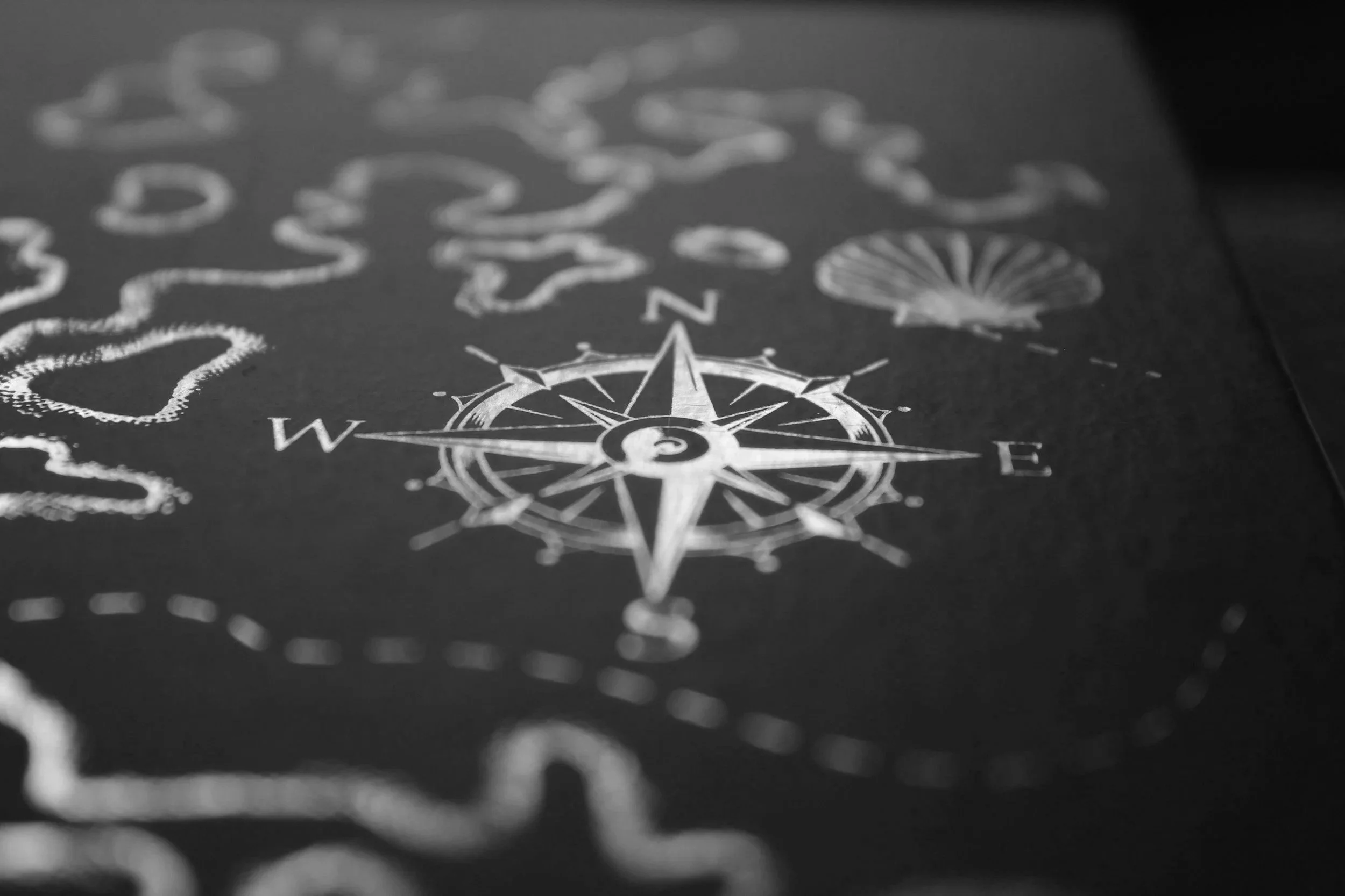 A black and white map with a compass rose and various dashed outline shapes of landmasses or islands.