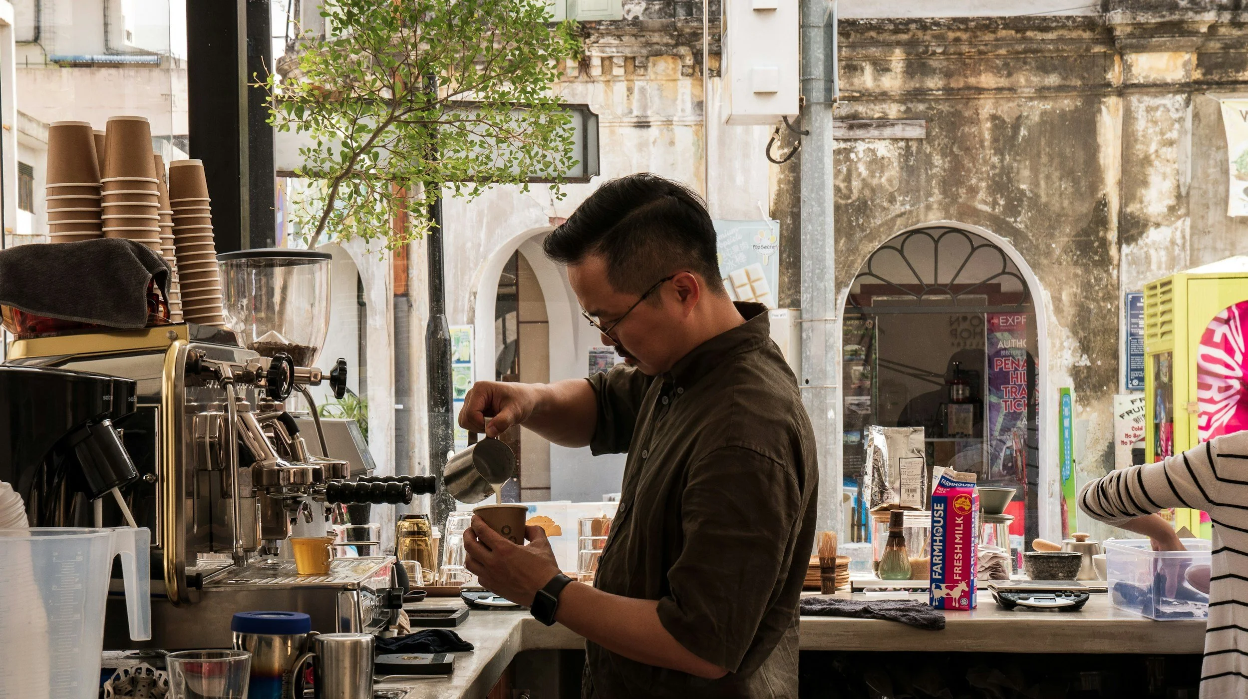 A man making coffee behind the counter at a cafe, pouring steamed milk into a cup.