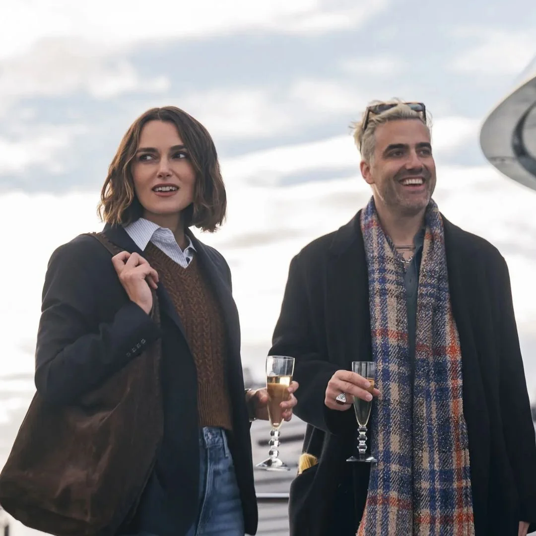 Two people celebrating outdoors with glasses of champagne, dressed in warm clothing, under a cloudy sky.