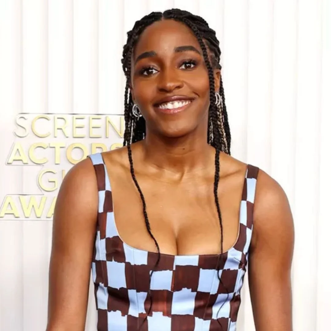 A smiling woman with braids in a checkered dress standing in front of a white background with some text.