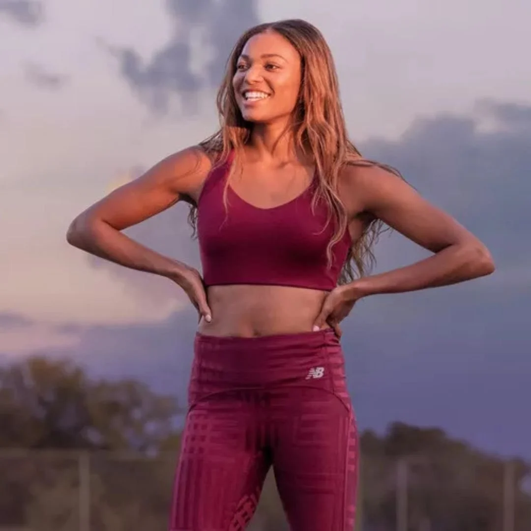 A woman standing outdoors in athletic wear, smiling with hands on her hips.