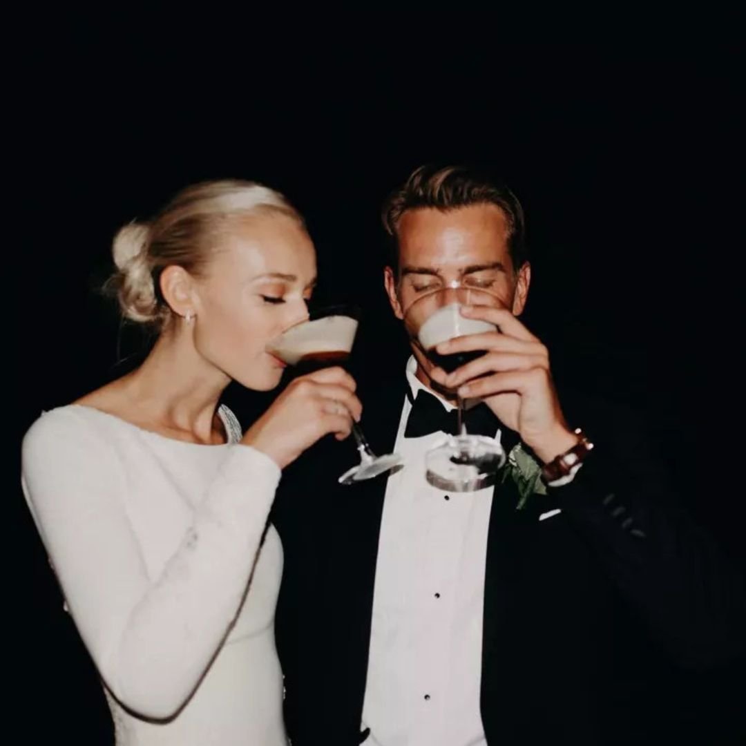 A man and woman in formal attire drinking cocktails together at a dark event.