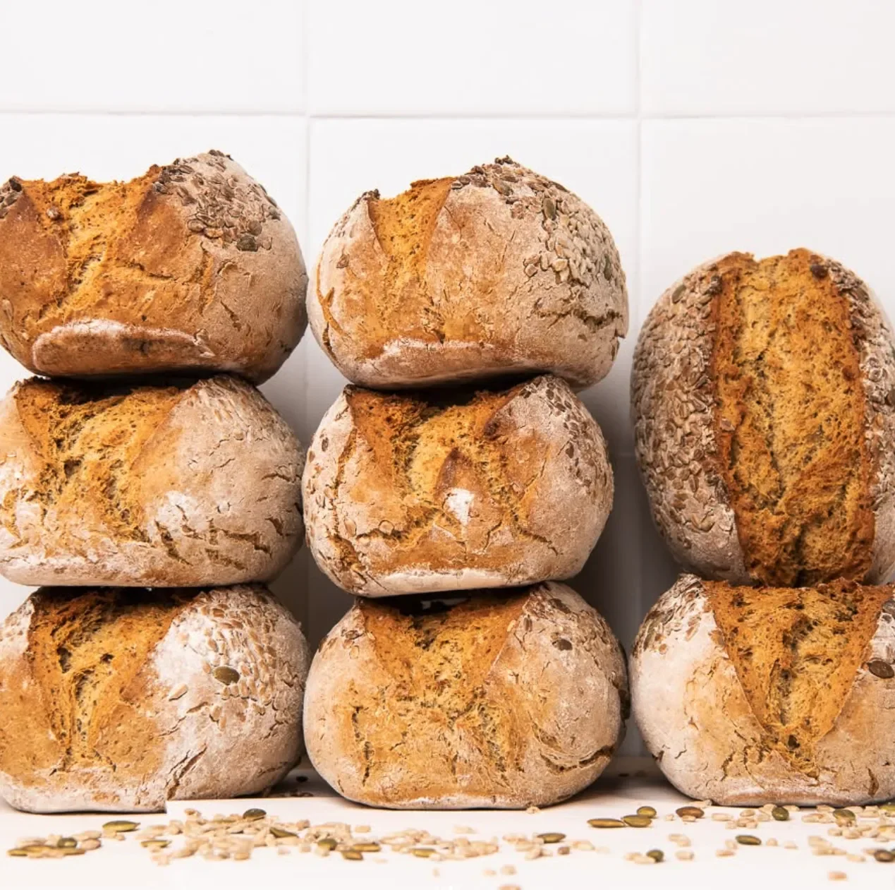 Stacked round bread rolls with cracked crusts and sprinkled seeds on top, set against a white background.