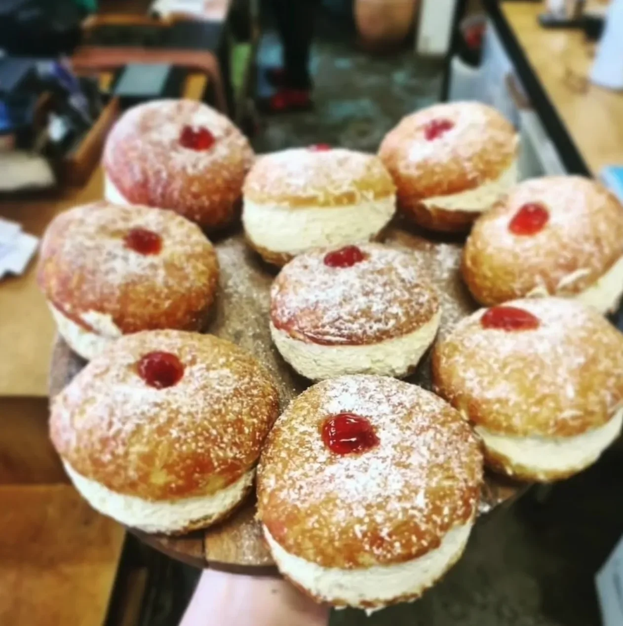 A plate of assorted donuts topped with powdered sugar and red jam centers at a bakery or café.