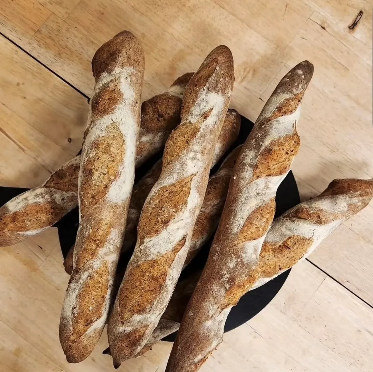 A basket of freshly baked baguettes with a dusting of flour on top, placed on a wooden surface.