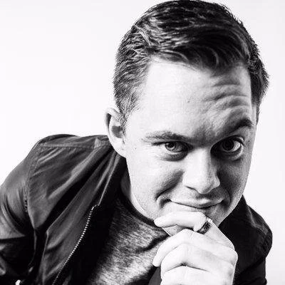NYC Footy's Morgan Collino. Black and white photo of a person wearing a leather jacket, looking into the camera, with hand near chin.