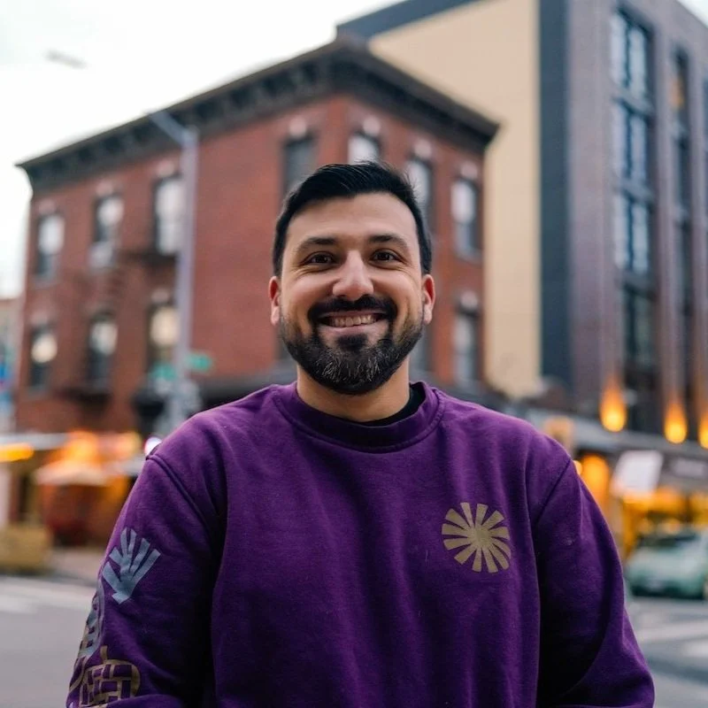 NYC Footy's Federico Zanatta. Smiling man in a purple sweater standing in front of brick building on a street corner.
