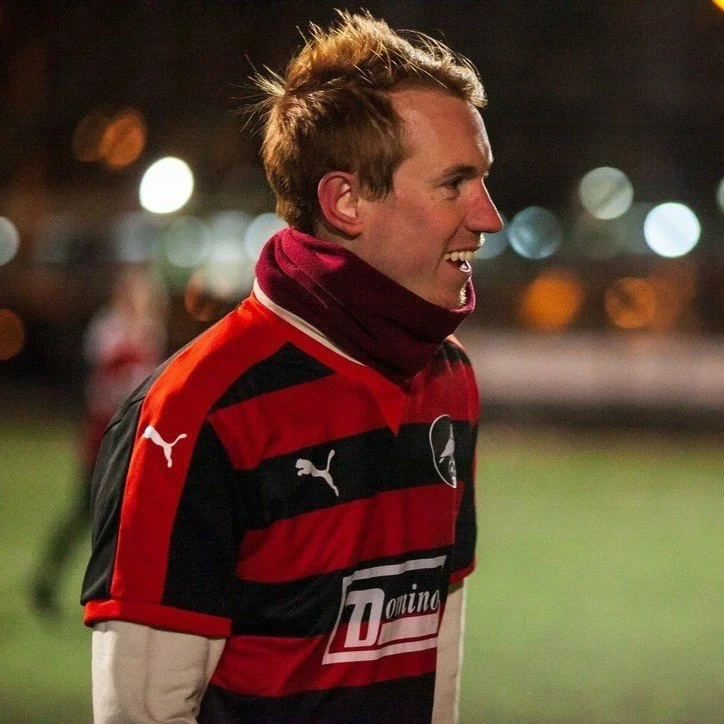 NYC Footy's Pat Seaward. Man in red and black striped sports jersey with Puma logo, outdoors at night.