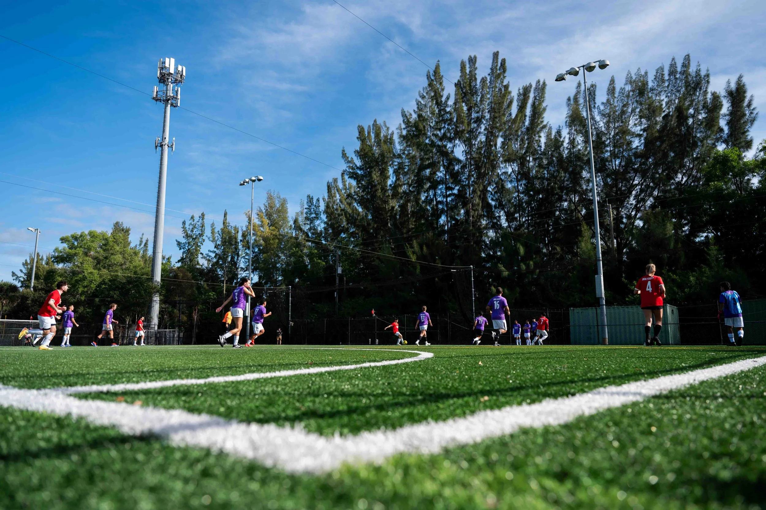 Tampa Bay Footy soccer players on a field during a game, with trees and blue sky in the background.