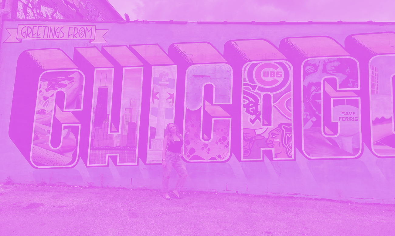 Woman standing in front of a large mural spelling 'CHICAGO' with cityscape and sports logos inside the letters, and a banner saying 'Greetings from' at the top.