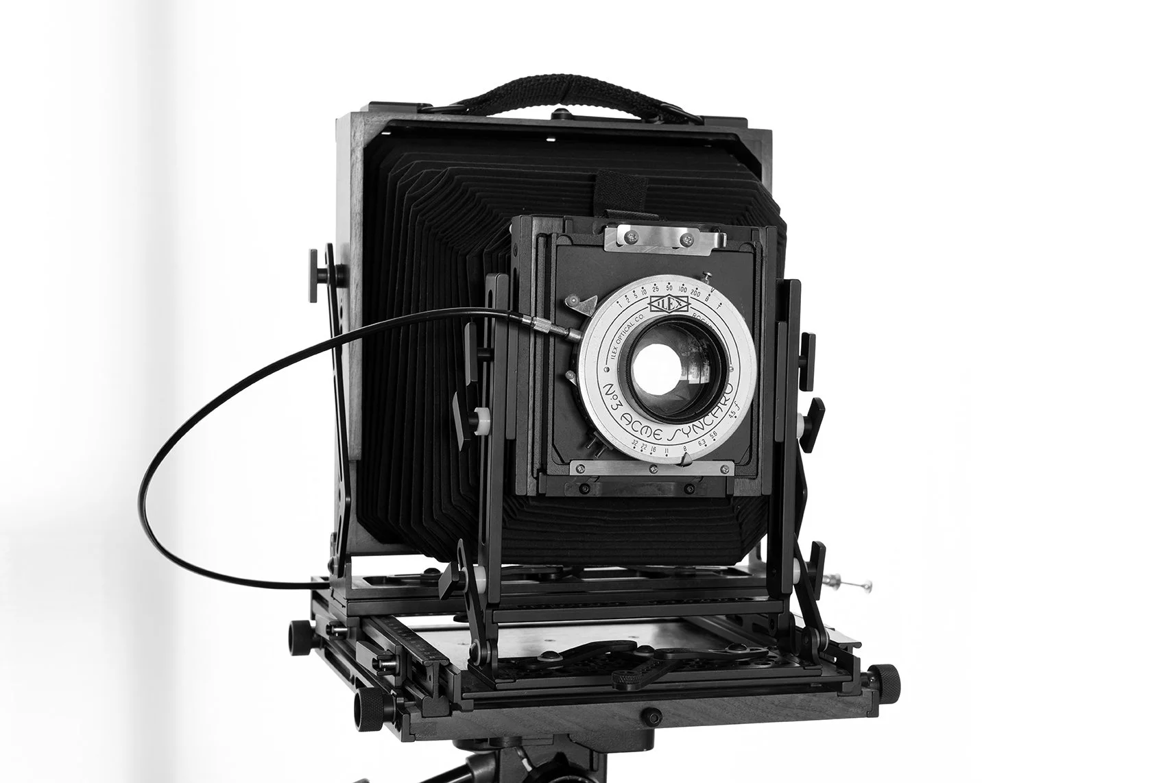 A large vintage large format wooden view camera with bellows and lens on a tripod