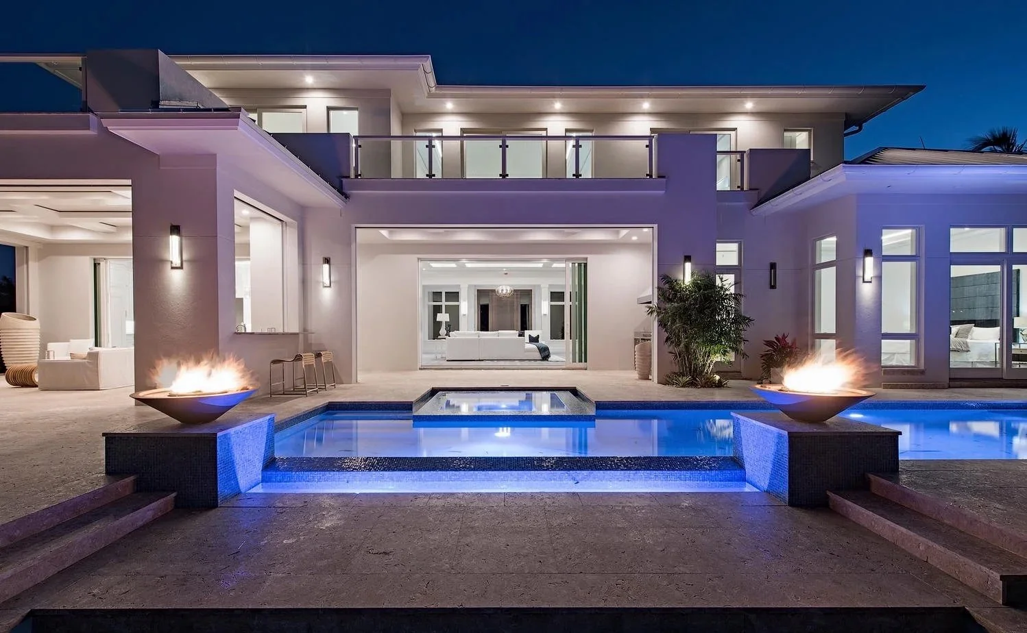 Modern house with illuminated swimming pool and fire bowls at night.