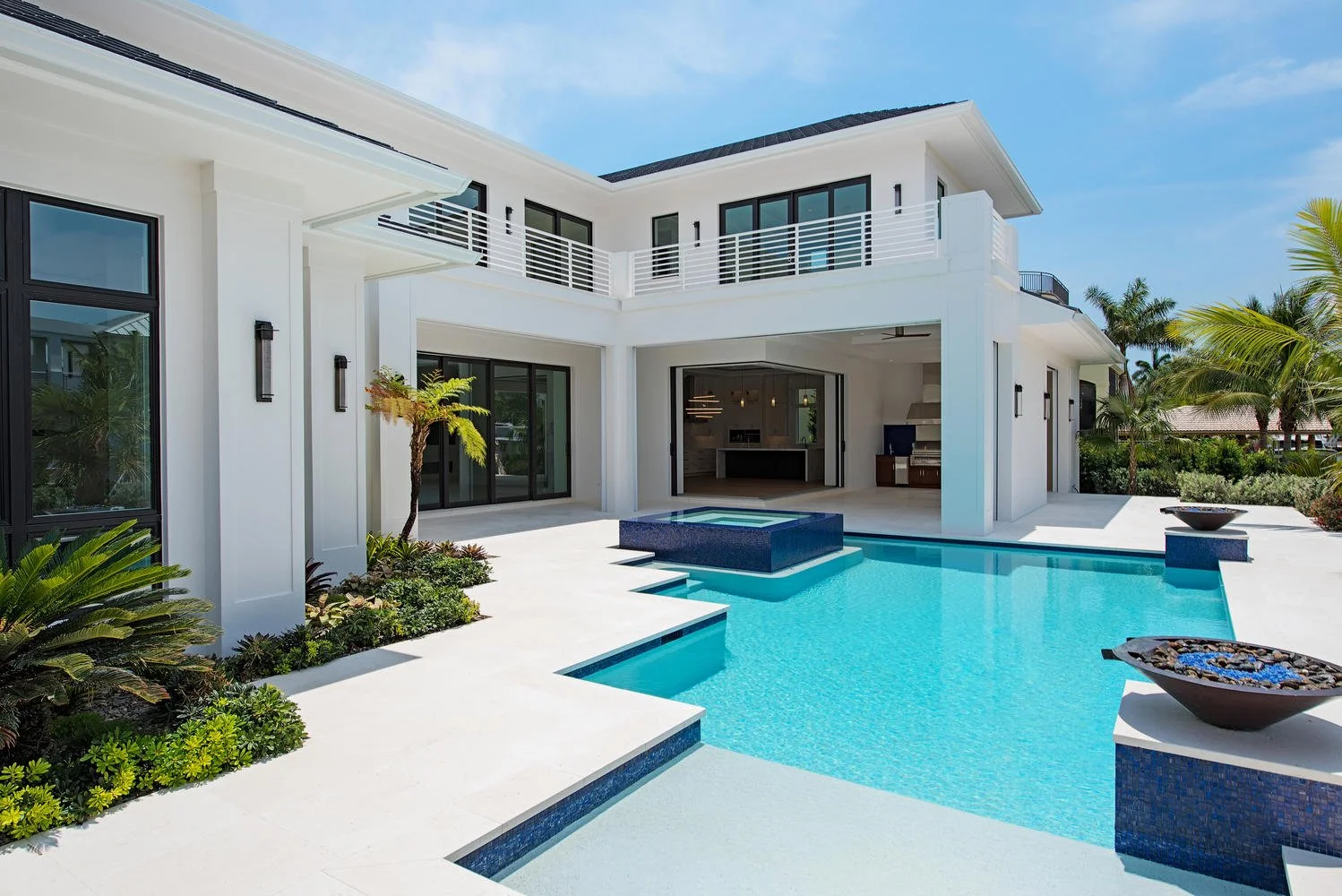 Modern white two-story house with large windows, a swimming pool, and surrounding greenery in a sunny outdoor setting.