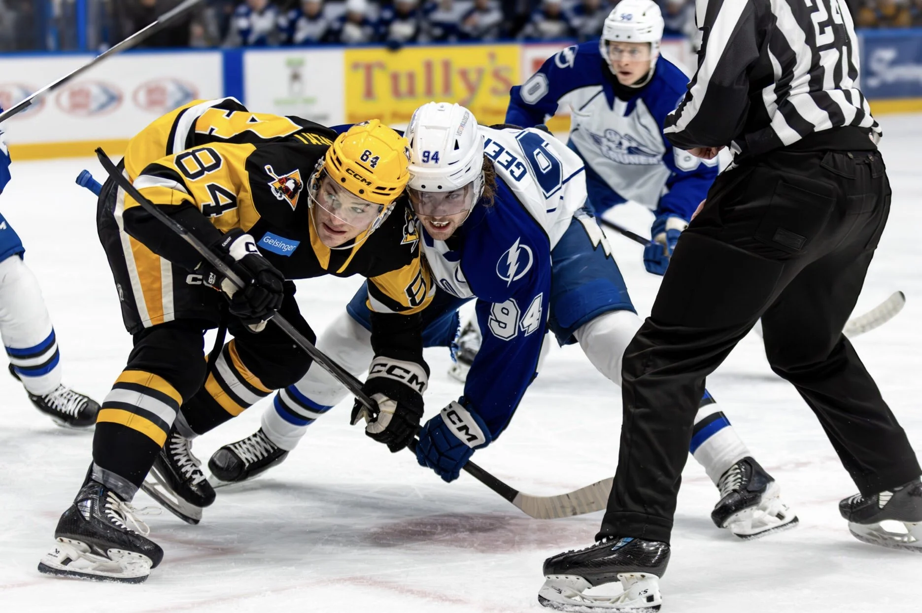 Ice hockey game with players from opposing teams fighting for control of the puck on the ice, with a referee nearby observing.