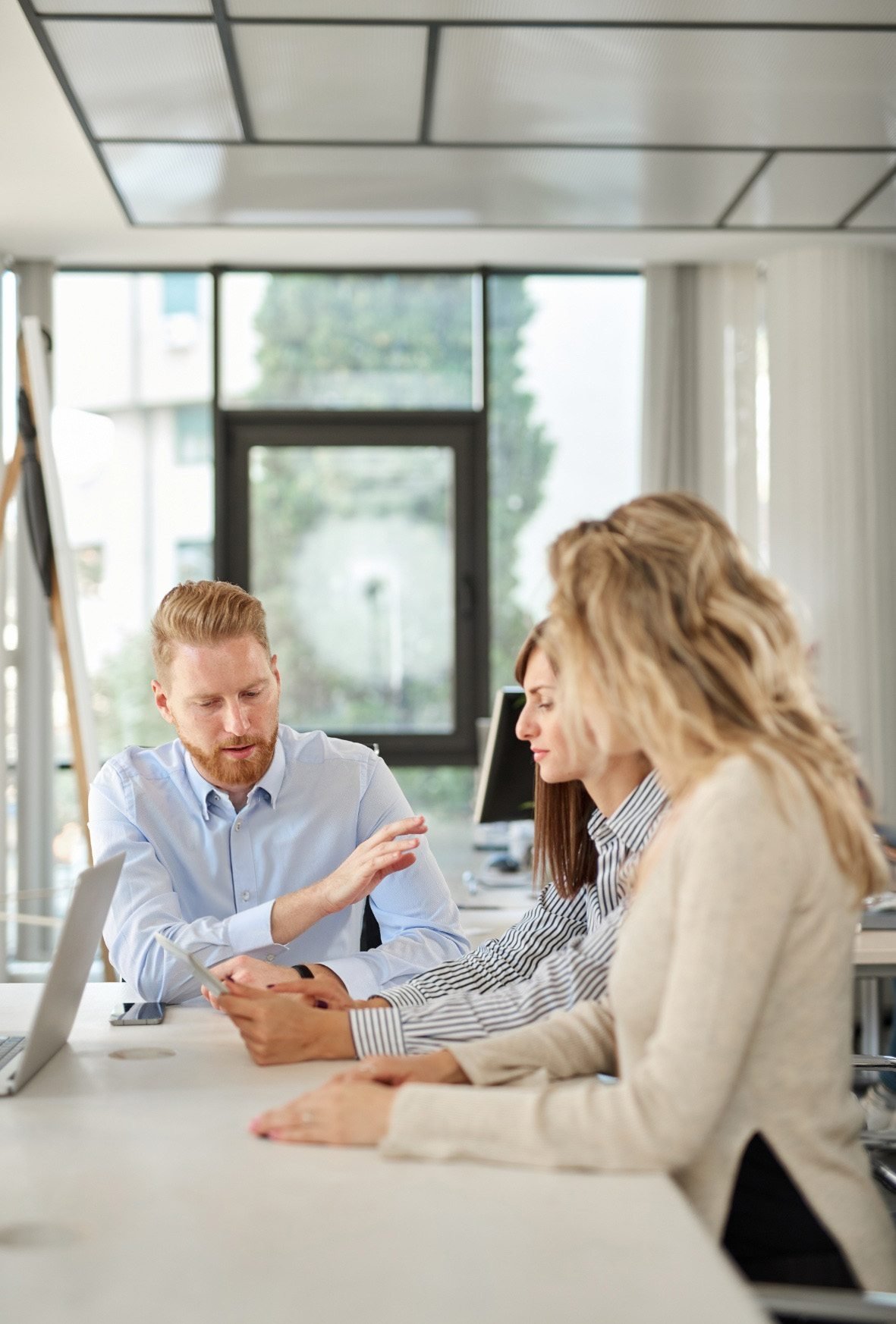 Group of four young professionals having a discussion in an office conference room with large windows.