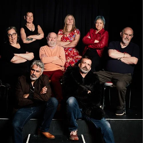 Eight adults posing together against a black backdrop, with six seated or standing behind two men on the floor.