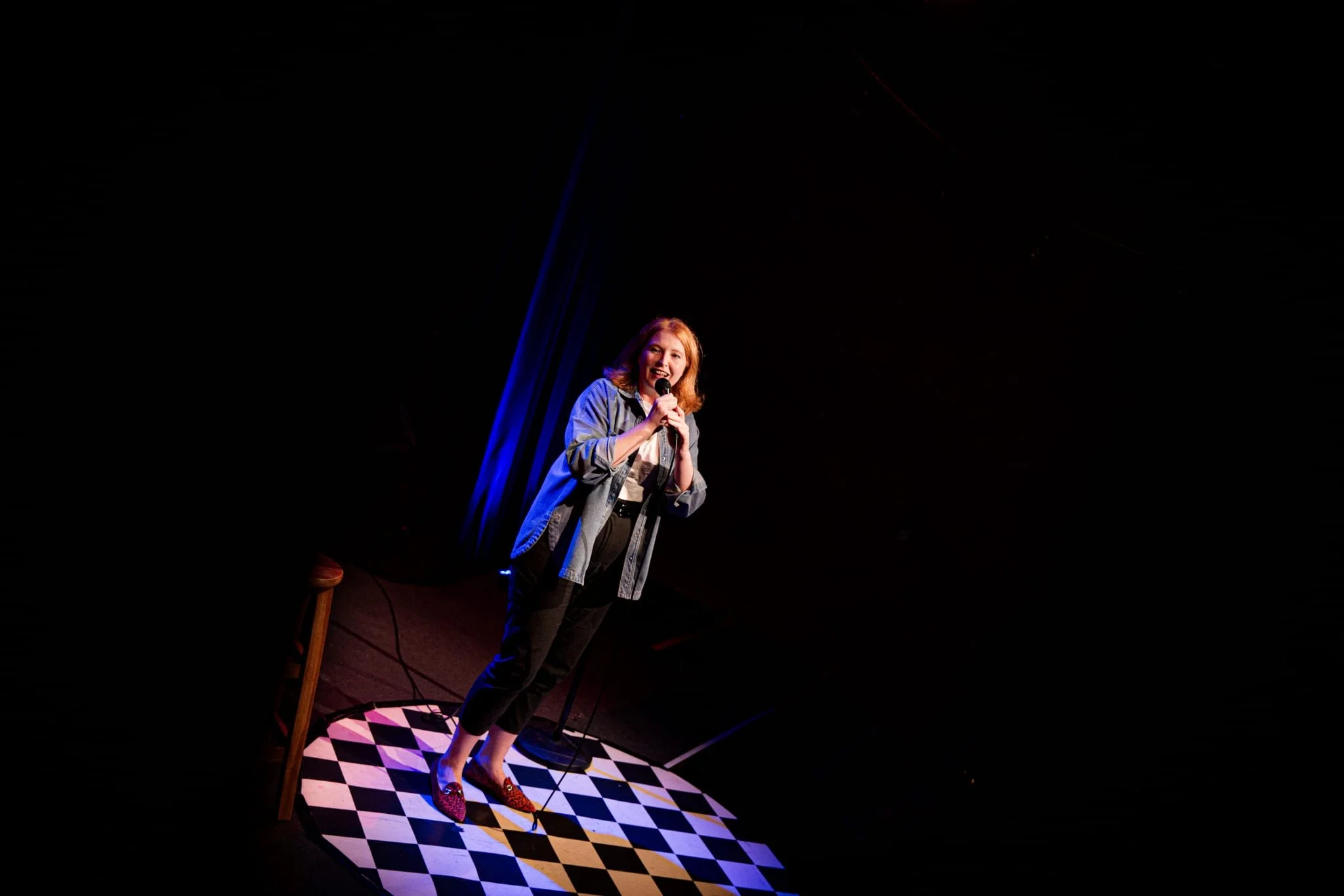 Comedian performing with a microphone on a checkerboard stage under blue and red lighting