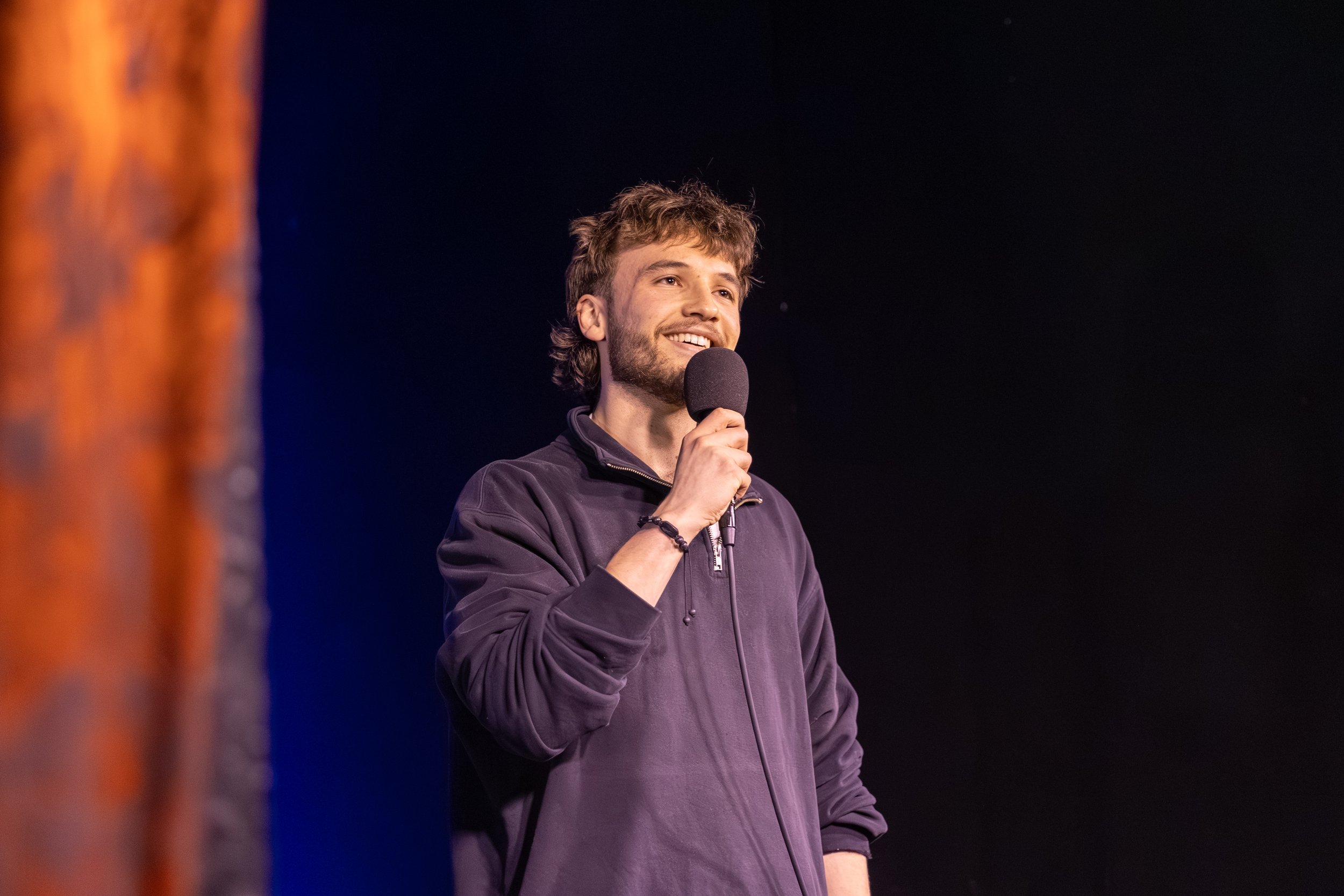 Smiling man speaking into a microphone on a dimly lit stage