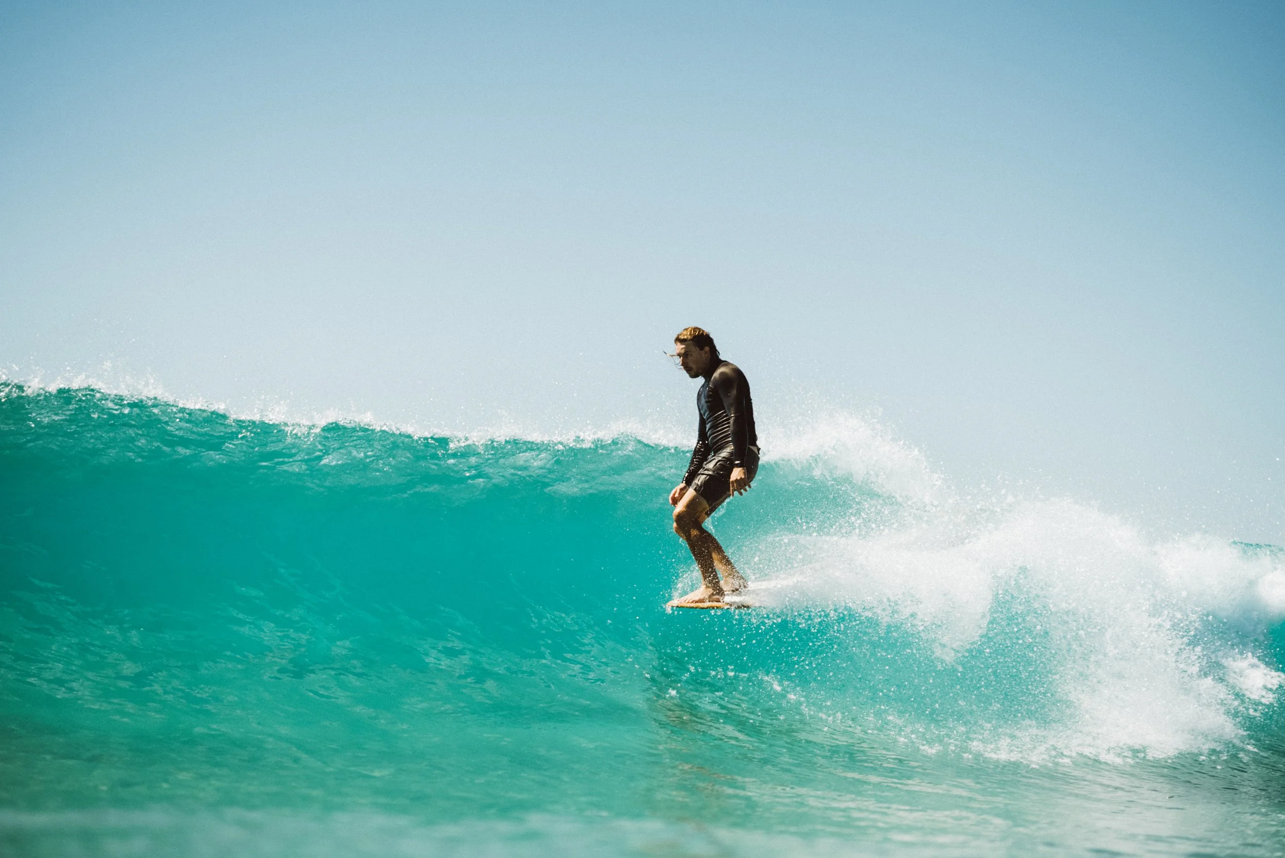 A man surfing on a turquoise wave under a clear blue sky.