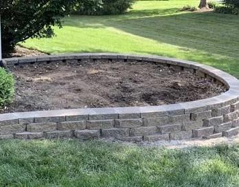 Curved brick retaining wall with soil inside, in a grassy yard.