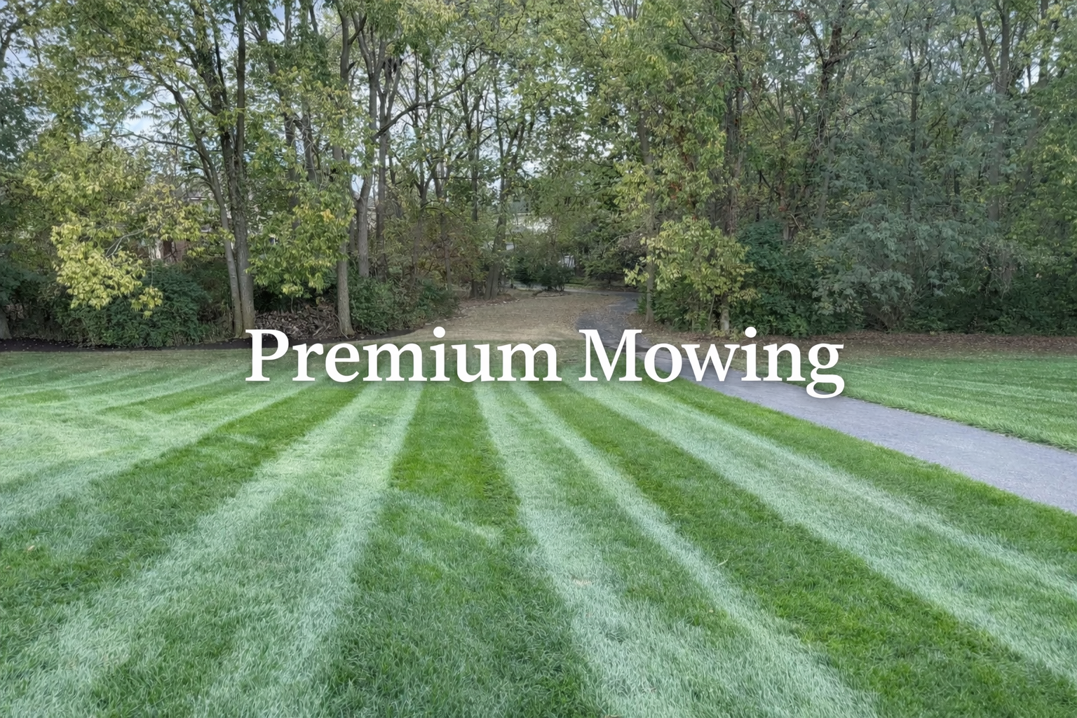 A well-maintained green lawn with striped grass, a pathway on the right, and trees in the background with the text 'Premium Mowing' overlaid.