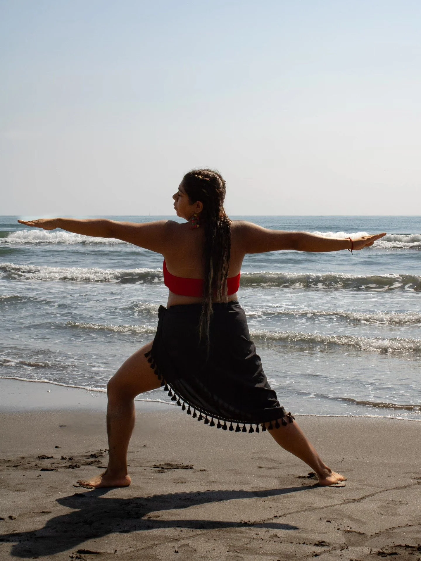 Mujer practicando yoga en la playa, en posición de guerrero, con el mar y el cielo de fondo