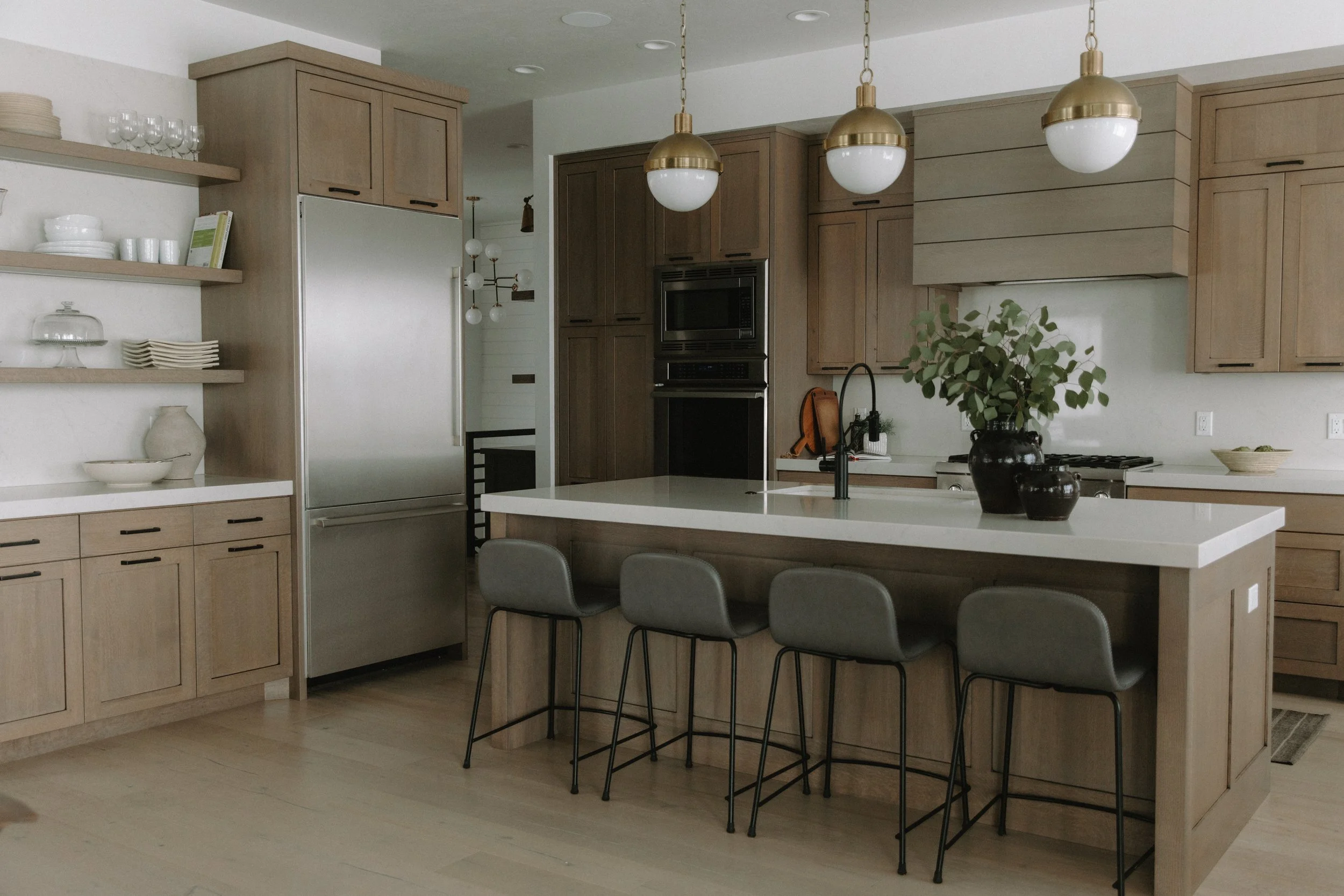 Warm and inviting organic kitchen with wood cabinetry, white countertops, gold pendant lighting, and a spacious island with bar seating.