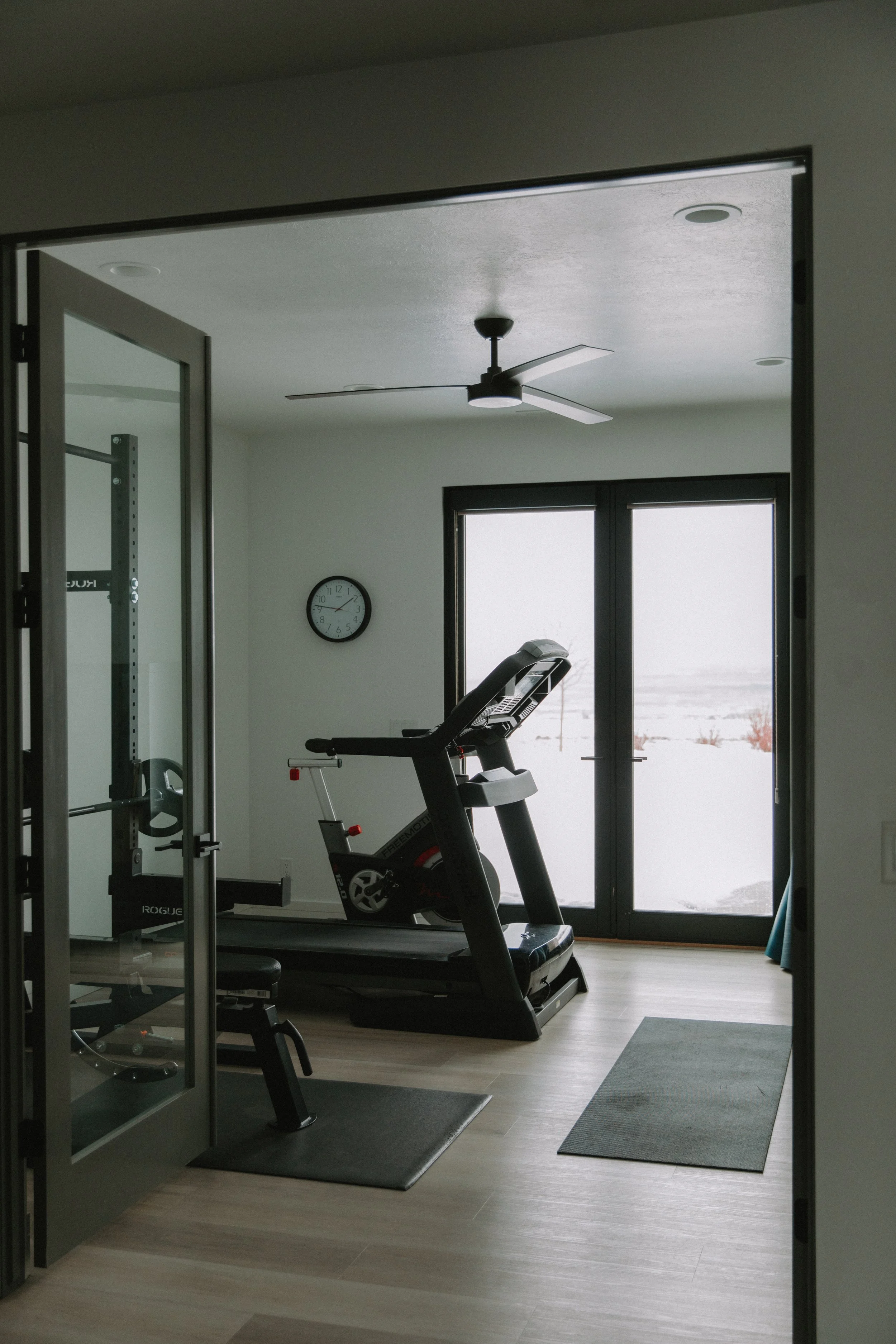 Home gym with a sleek glass partition, black exercise equipment, and large windows allowing for natural light