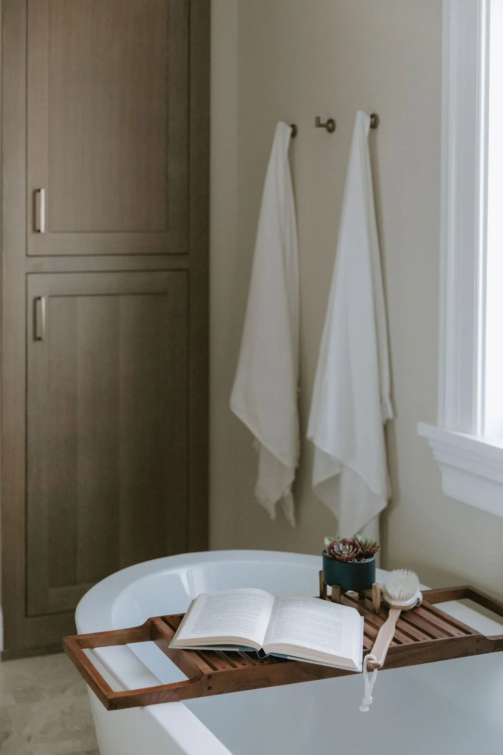 Freestanding bathtub with a built-in wood storage cabinet, gold fixtures, and soft neutral textures for a tranquil spa feel.