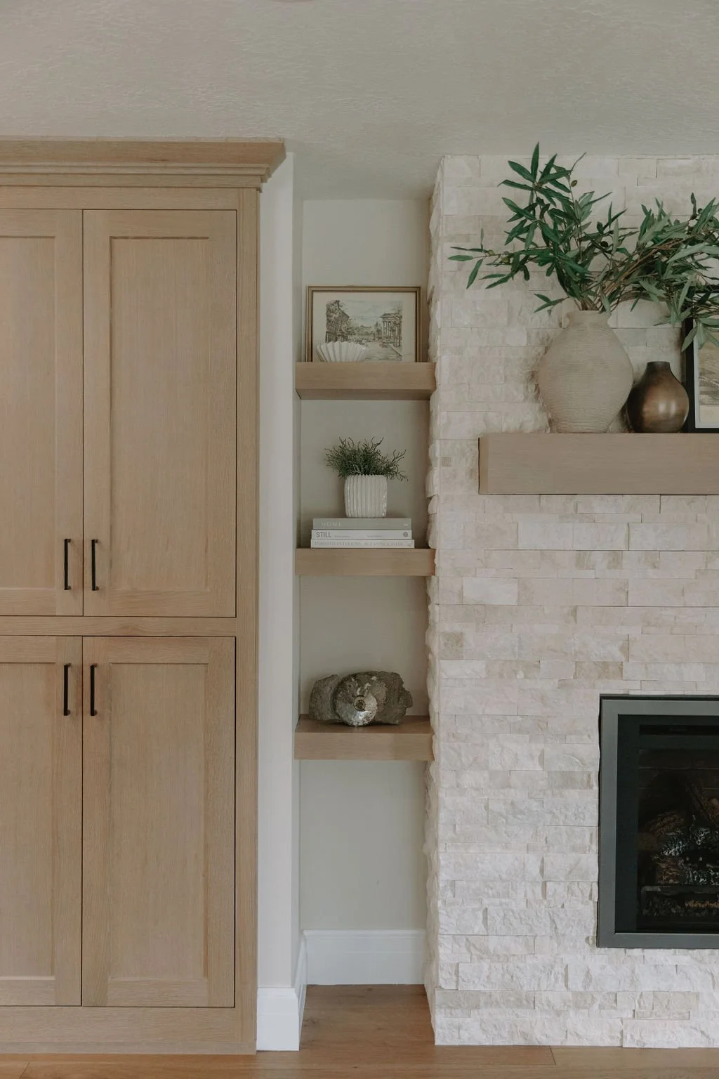 Built-in cabinetry and stone fireplace with floating wood shelves, featuring organic decor and a warm, inviting aesthetic.