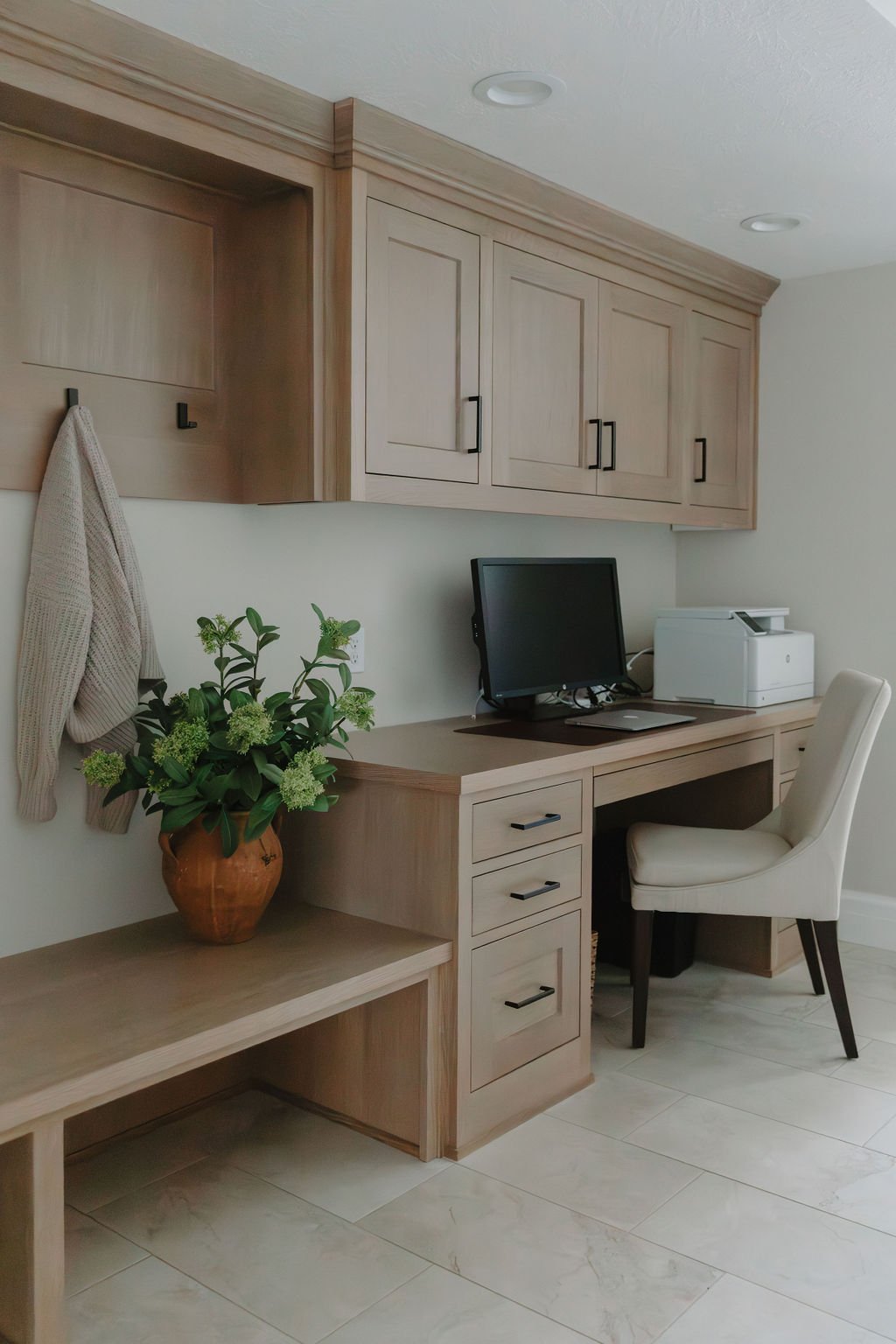 Home office with built-in wood cabinetry, a spacious desk, and a cozy upholstered chair for a functional workspace.
