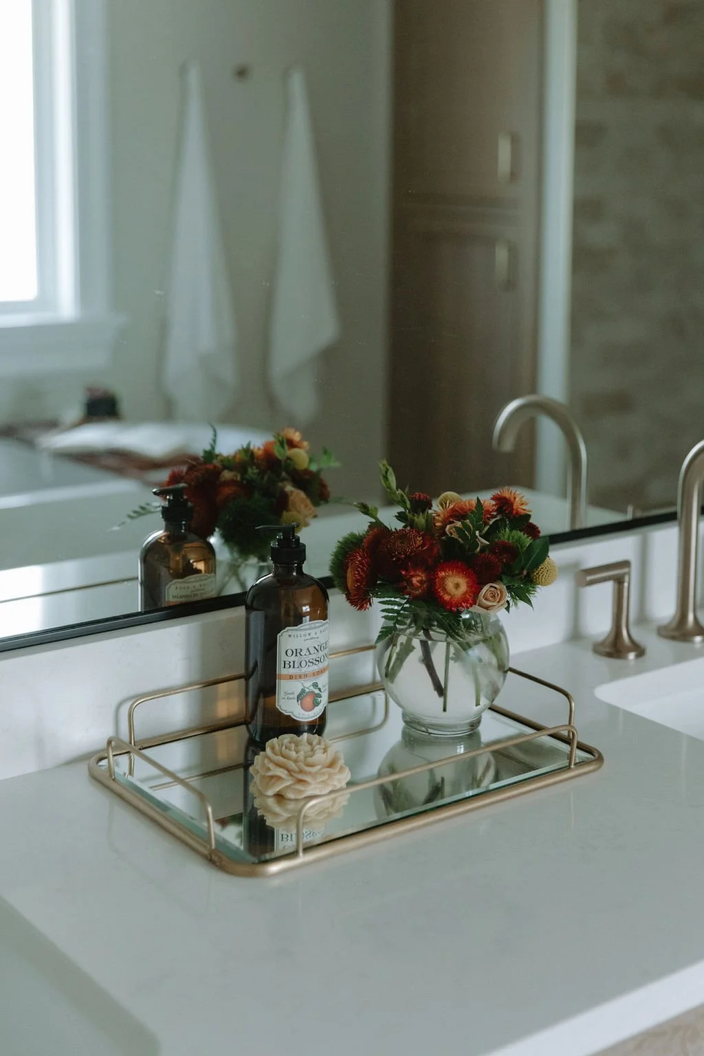 Elegant bathroom vanity styled with a gold tray, fresh floral arrangement, and amber glass soap dispensers for a spa-like touch.