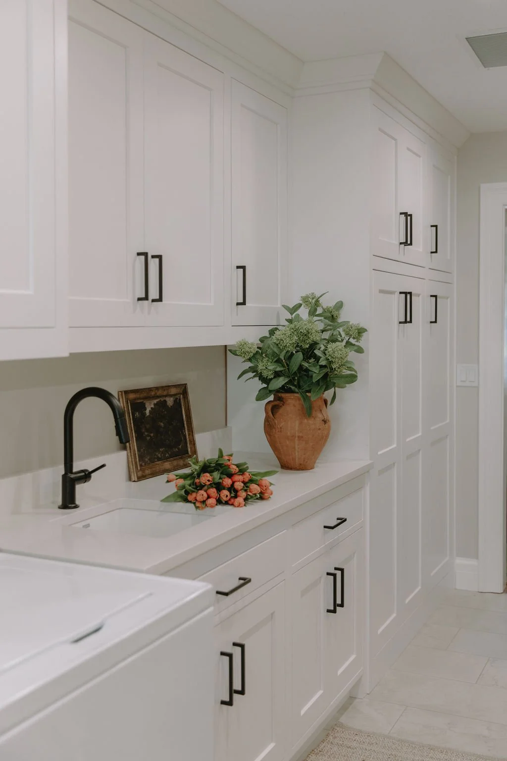 Bright and spacious laundry room with white shaker cabinets, black hardware, and a farmhouse sink with a matte black faucet.