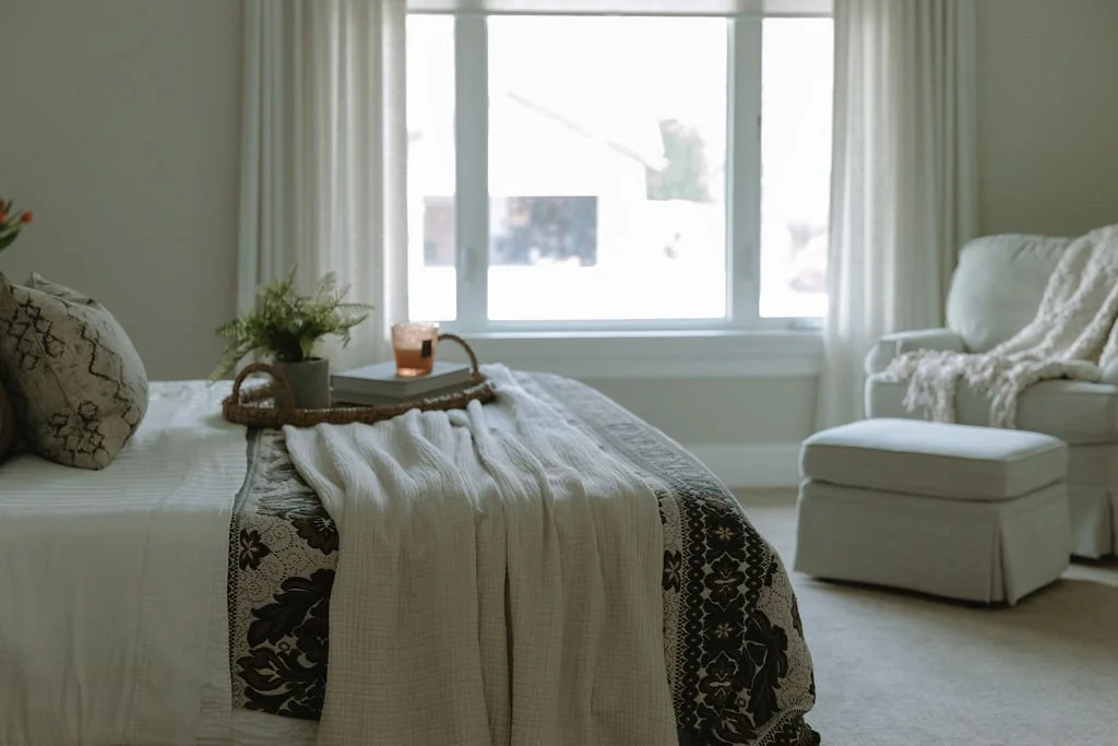 Close-up of a styled bed with soft linens, a woven tray, fresh greenery, and a candle for a relaxing retreat.