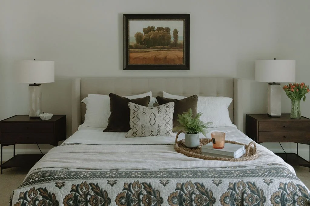 Elegant bed set up with plush pillows and patterned throw blanket and framed landscape painting for a serene atmosphere.