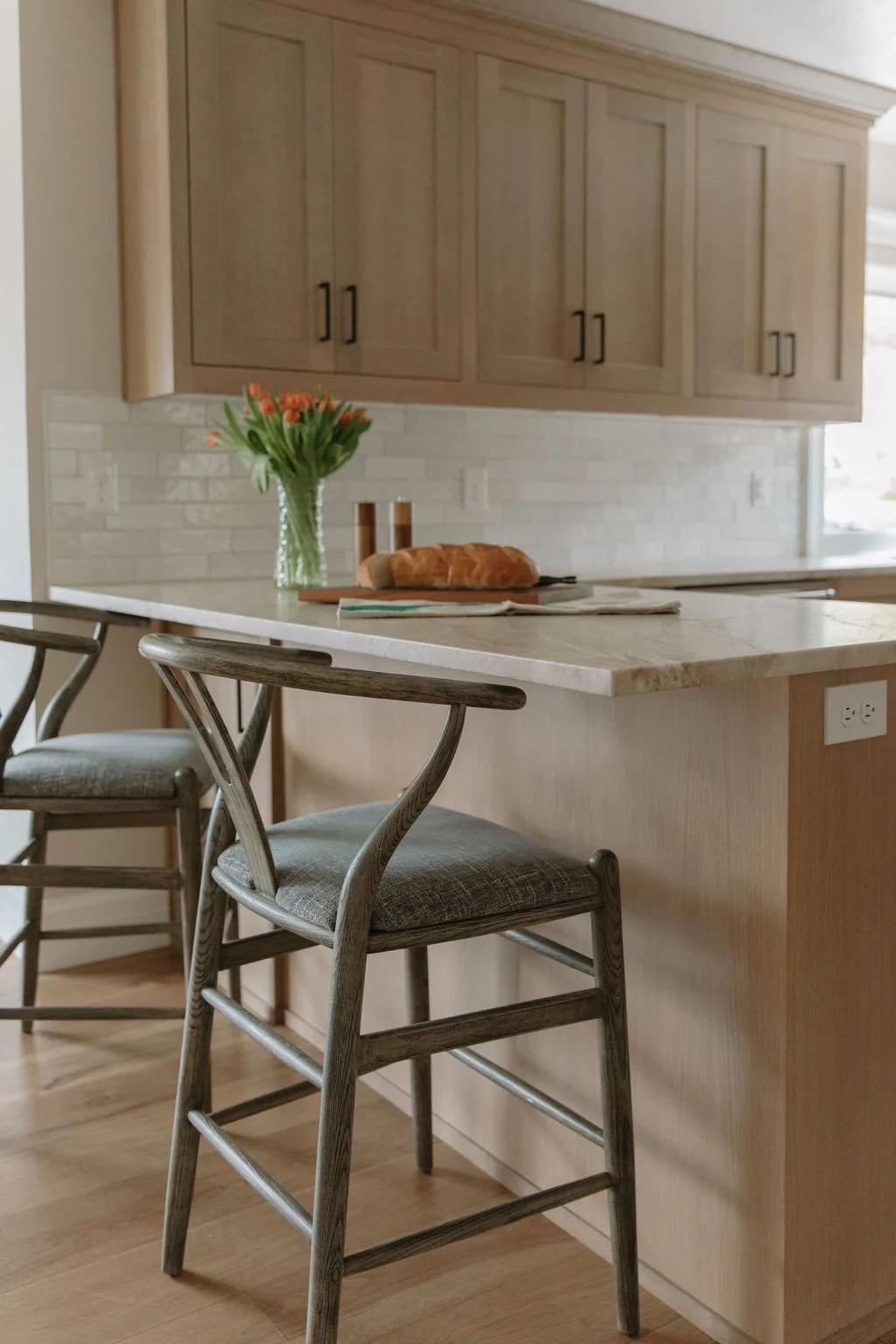 Kitchen island with wood barstools, soft neutral tones, and a subway tile backsplash enhancing the transitional design.