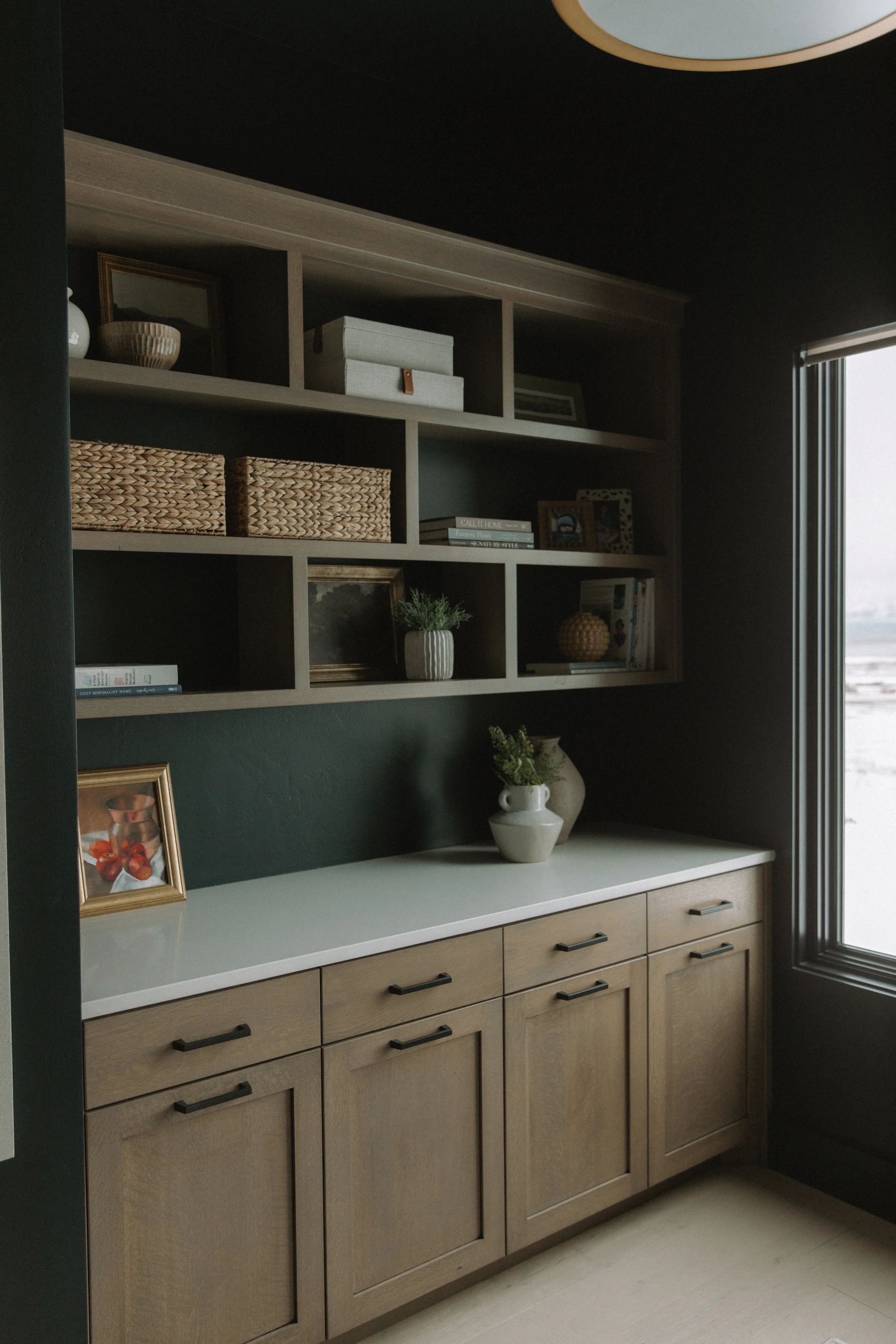 Office shelving above drawers filled with baskets, paintings, and plants