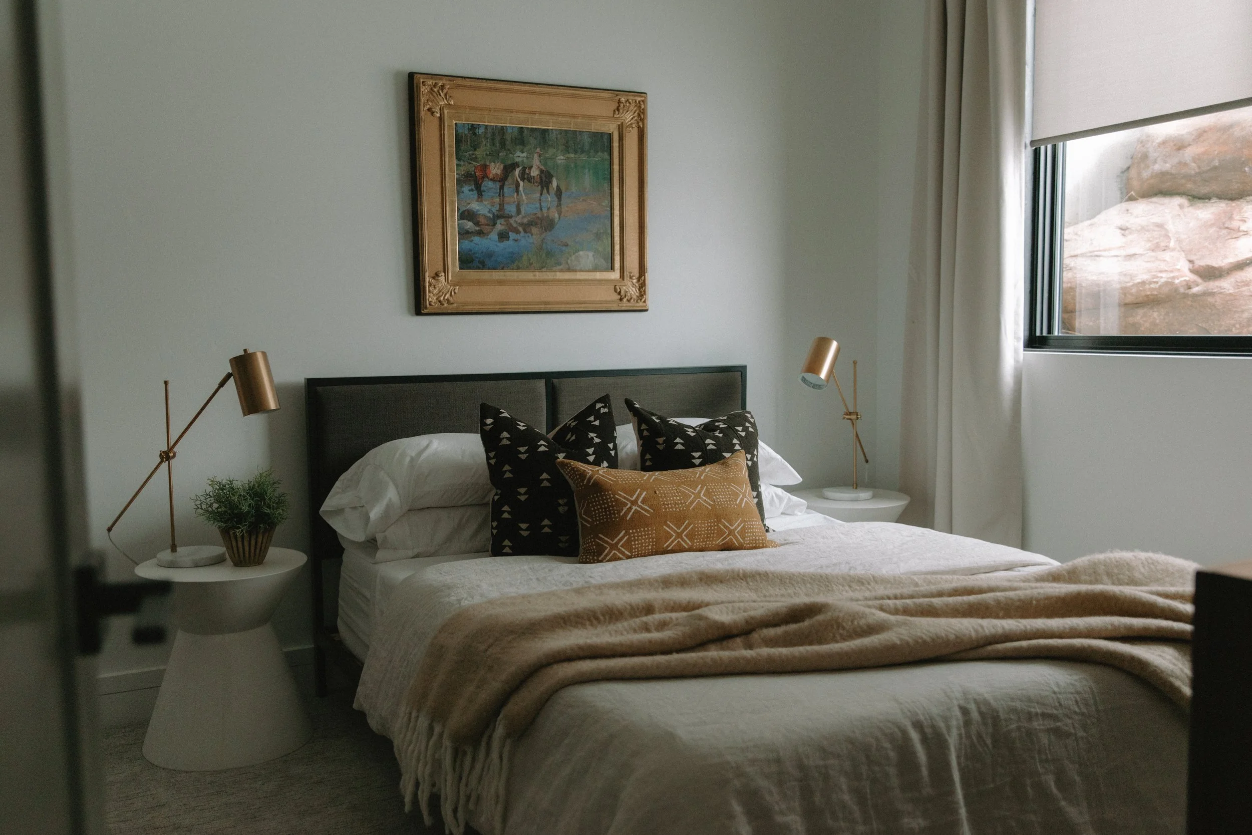 King-size bed with linen bedding, textured decorative pillows, modern night stands and painting of nature-scene hanging above bed