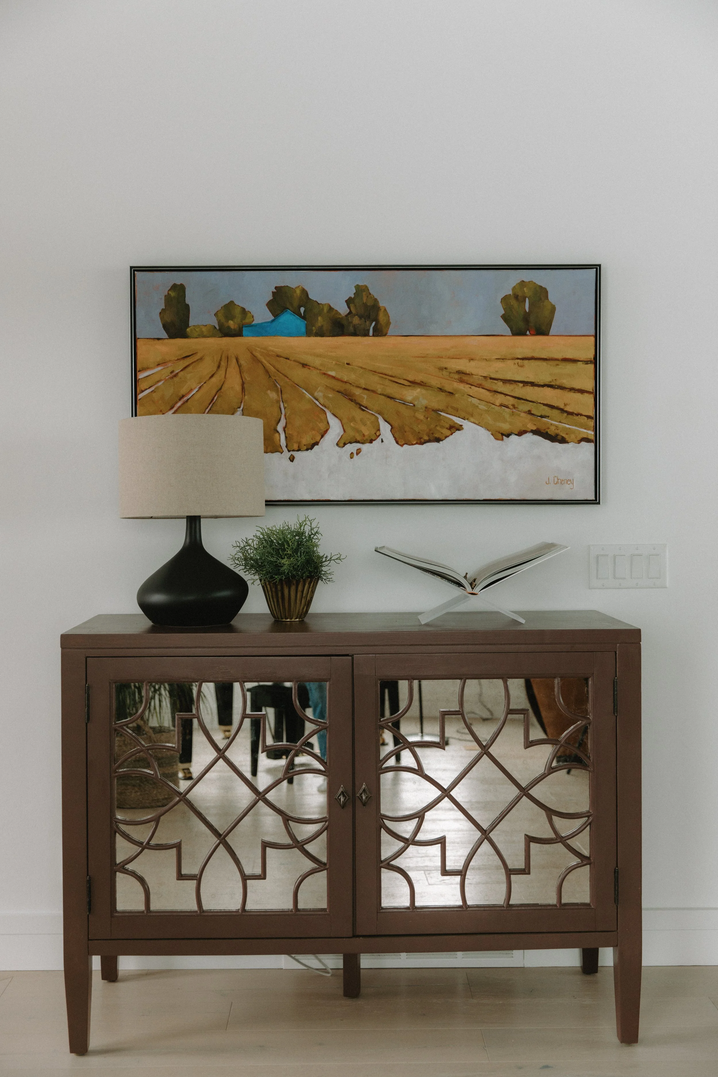 Entryway cabinet decorated with table lamp, plant and painting hanging of a farm field