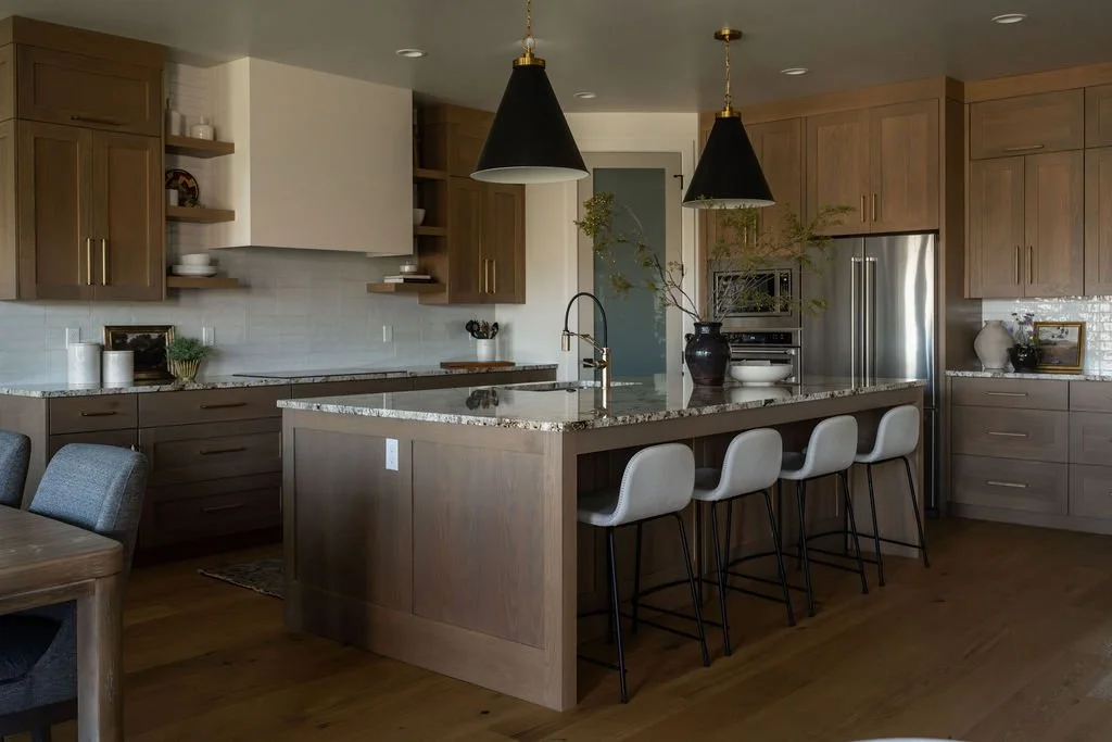 Luxury kitchen with warm wood cabinetry, granite countertops, and black pendant lighting over a spacious island with upholstered barstools.